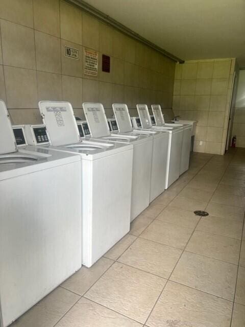 laundry room featuring light tile patterned flooring, tile walls, and washing machine and dryer