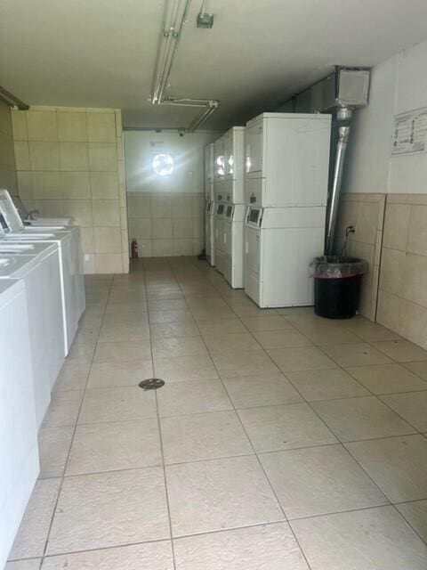 clothes washing area with stacked washer and dryer, tile walls, washing machine and clothes dryer, and light tile patterned floors