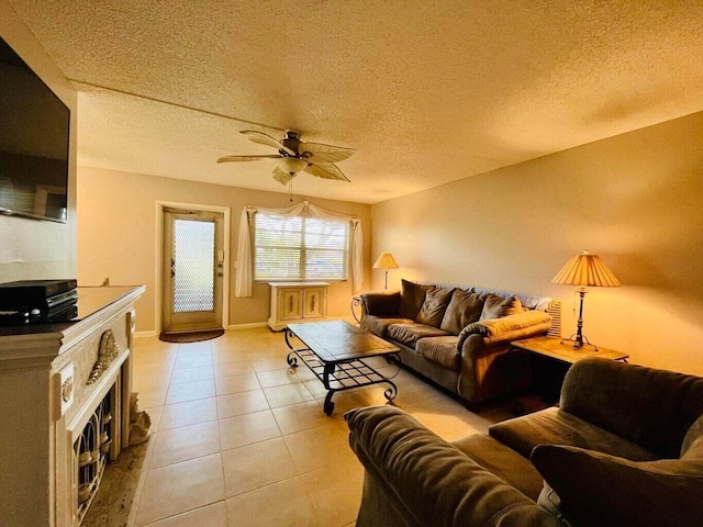 living room featuring ceiling fan, a textured ceiling, light tile patterned flooring, a fireplace, and baseboards