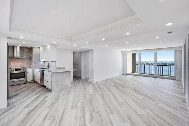 kitchen featuring white cabinets, appliances with stainless steel finishes, light hardwood / wood-style floors, wall chimney range hood, and a water view