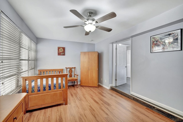 bedroom with ceiling fan, a nursery area, and light hardwood / wood-style flooring