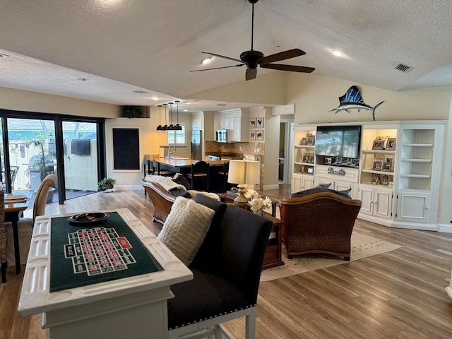 dining space with ceiling fan, vaulted ceiling, a textured ceiling, and light wood-type flooring