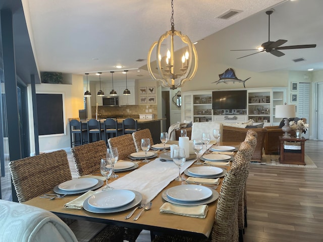 dining room featuring dark wood-type flooring, lofted ceiling, ceiling fan with notable chandelier, and a textured ceiling