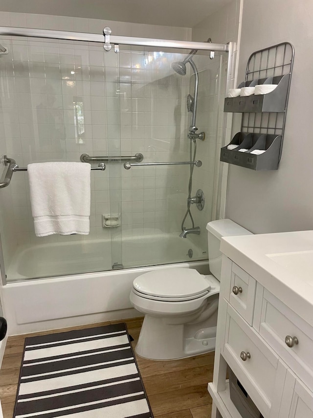 full bathroom featuring hardwood / wood-style flooring, enclosed tub / shower combo, vanity, and toilet