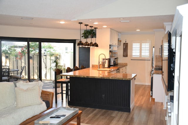 kitchen with white cabinetry, sink, a kitchen bar, hanging light fixtures, and kitchen peninsula