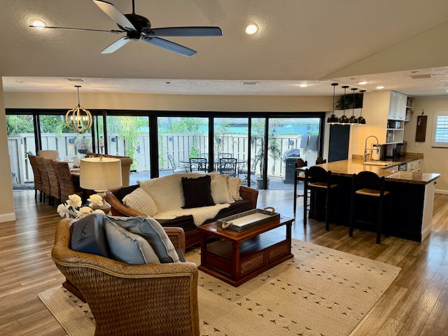 living room featuring lofted ceiling, ceiling fan with notable chandelier, light hardwood / wood-style flooring, and a textured ceiling