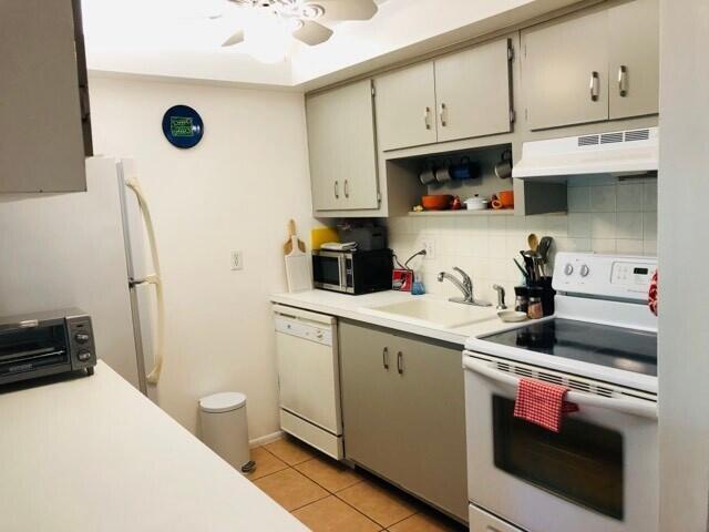 kitchen with light tile patterned floors, under cabinet range hood, white appliances, a sink, and decorative backsplash