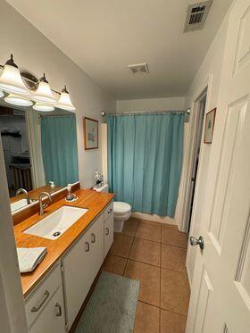 full bath featuring toilet, tile patterned floors, visible vents, vanity, and shower / tub combo with curtain