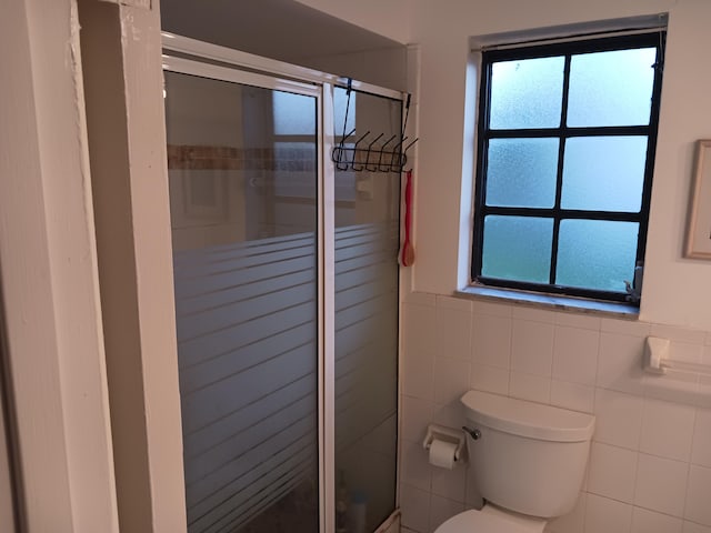 bathroom featuring a shower with door, toilet, and tile walls