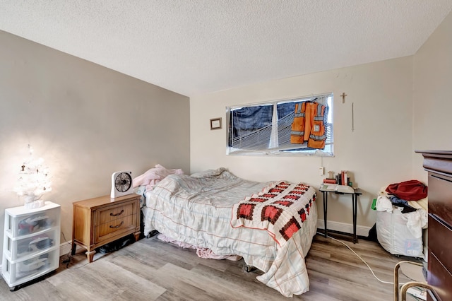 bedroom featuring a textured ceiling, baseboards, and wood finished floors