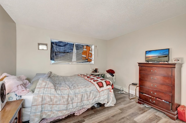 bedroom featuring baseboards, a textured ceiling, and wood finished floors