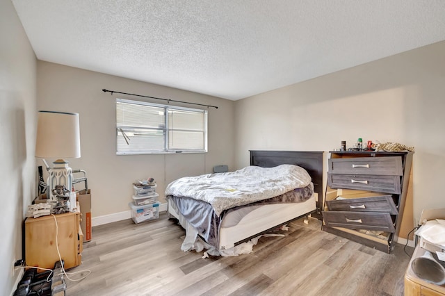 bedroom featuring light wood finished floors, a textured ceiling, and baseboards