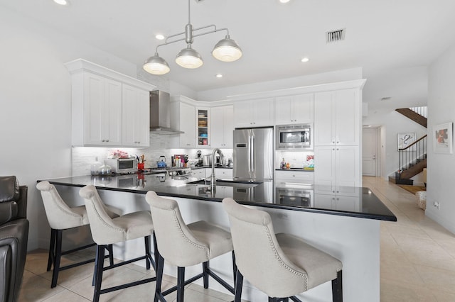 kitchen featuring wall chimney range hood, light tile flooring, stainless steel appliances, backsplash, and white cabinets