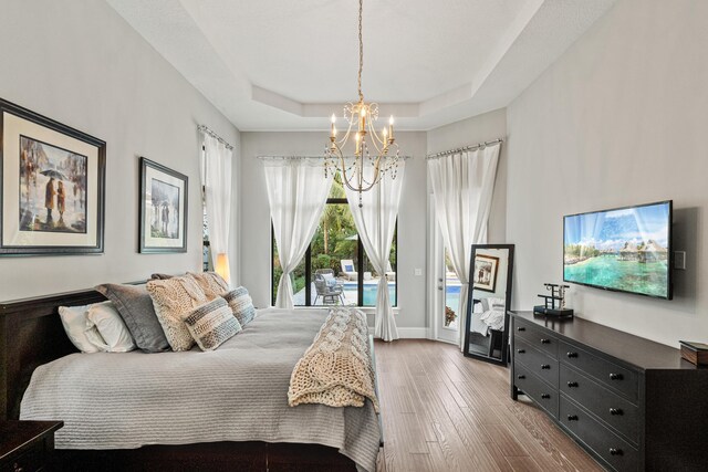 bedroom featuring a tray ceiling, an inviting chandelier, access to outside, and wood-type flooring