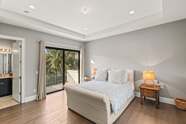 bedroom with a tray ceiling, connected bathroom, access to exterior, and hardwood / wood-style flooring