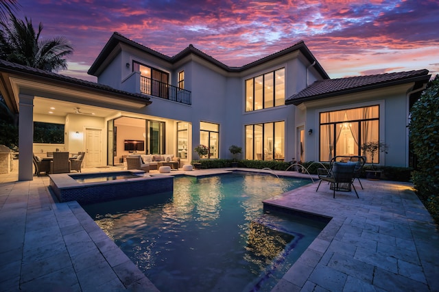 back house at dusk featuring a balcony, an outdoor living space, pool water feature, and a patio