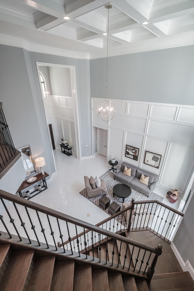 living room with a towering ceiling, coffered ceiling, a notable chandelier, and wood-type flooring