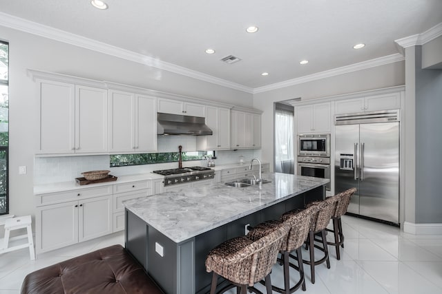 kitchen with decorative backsplash, built in appliances, an island with sink, sink, and crown molding