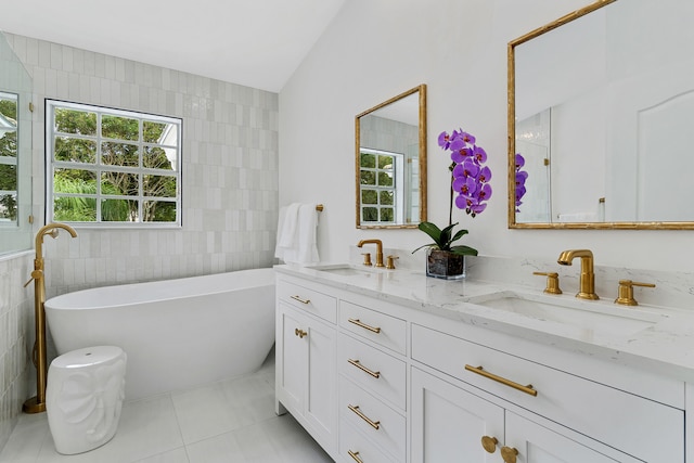 bathroom with dual bowl vanity, tile walls, a bath, and tile patterned flooring