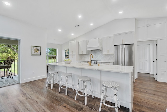 kitchen featuring lofted ceiling, custom range hood, a center island with sink, stainless steel appliances, and wood-type flooring