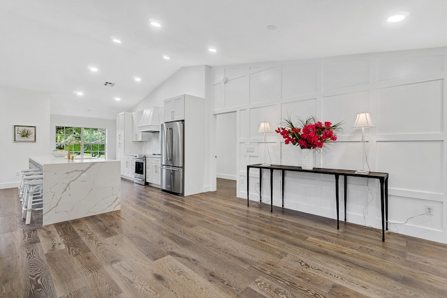 kitchen featuring appliances with stainless steel finishes, light stone counters, premium range hood, wood-type flooring, and white cabinets