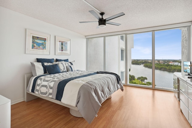 bedroom featuring ceiling fan, access to exterior, light wood-type flooring, a textured ceiling, and a wall of windows