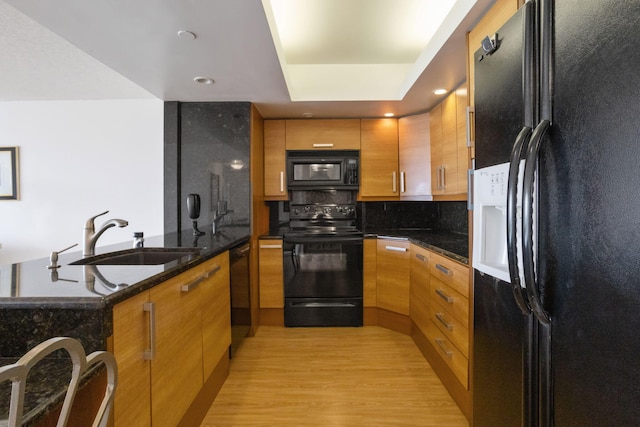 kitchen with backsplash, dark stone counters, black appliances, sink, and light hardwood / wood-style floors