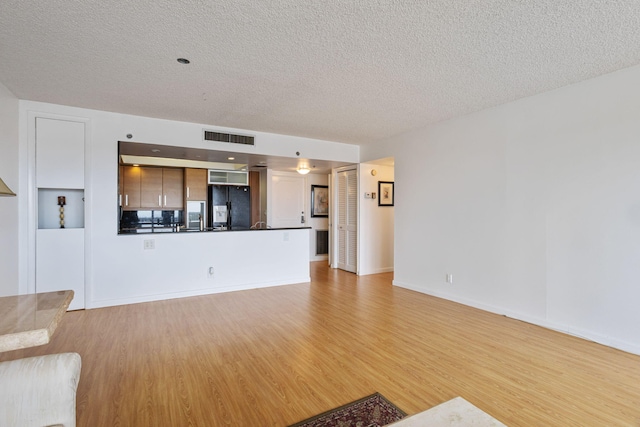 unfurnished living room with a textured ceiling and light hardwood / wood-style floors