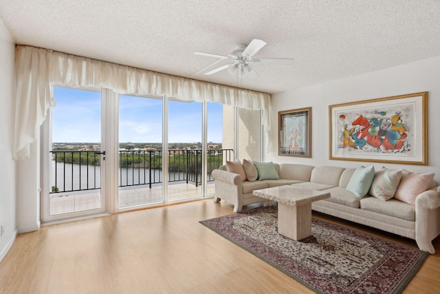 living room featuring ceiling fan, light hardwood / wood-style floors, a water view, and a textured ceiling