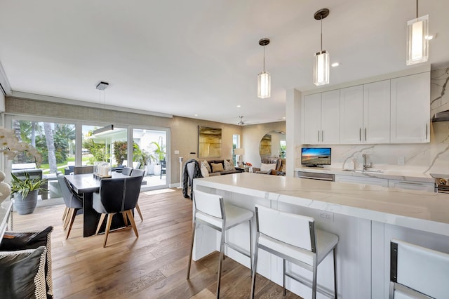 kitchen with light stone countertops, hanging light fixtures, light hardwood / wood-style floors, white cabinets, and sink