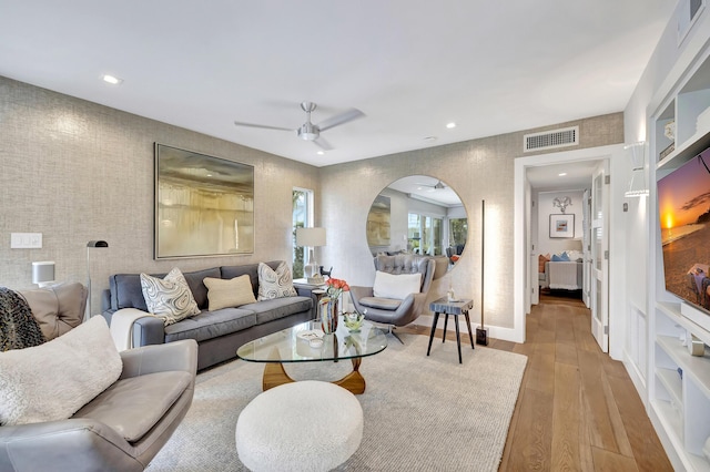 living room with built in features, ceiling fan, and hardwood / wood-style floors