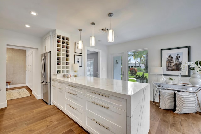 kitchen featuring white cabinetry, kitchen peninsula, stainless steel refrigerator, light stone countertops, and pendant lighting