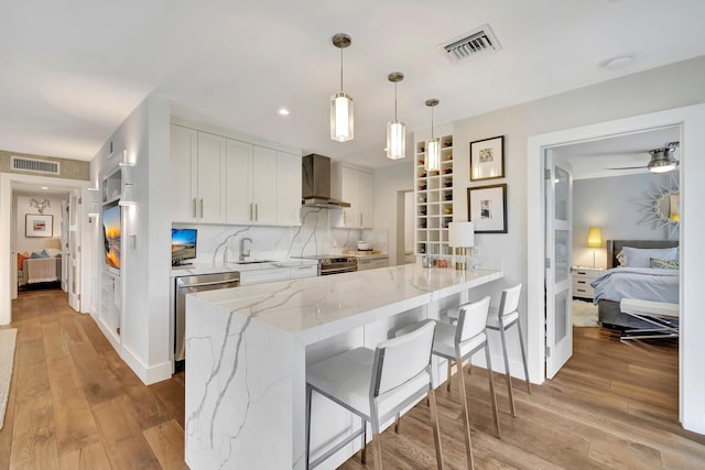 kitchen featuring stainless steel appliances, white cabinetry, decorative light fixtures, and wall chimney exhaust hood