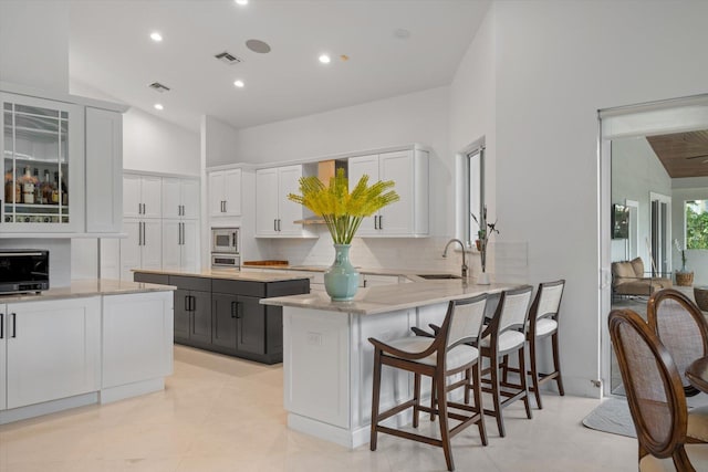 kitchen featuring stainless steel microwave, a breakfast bar area, sink, a center island, and white cabinetry