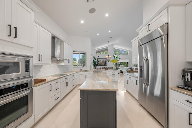 kitchen with lofted ceiling, white cabinetry, built in appliances, wall chimney exhaust hood, and a center island