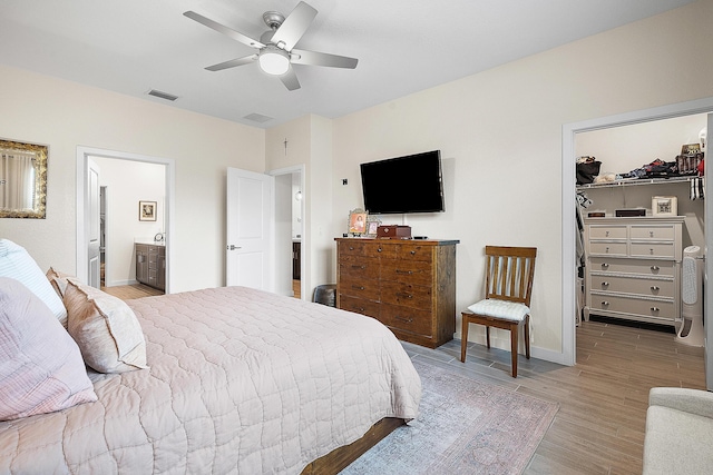 bedroom featuring ceiling fan, light wood-type flooring, a closet, a walk in closet, and ensuite bath