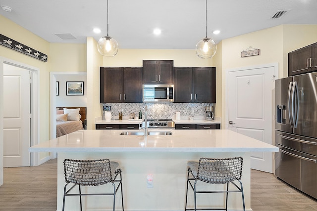 kitchen with stainless steel appliances, decorative light fixtures, a kitchen breakfast bar, and an island with sink