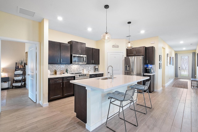 kitchen featuring a kitchen island with sink, a breakfast bar area, appliances with stainless steel finishes, sink, and light hardwood / wood-style flooring