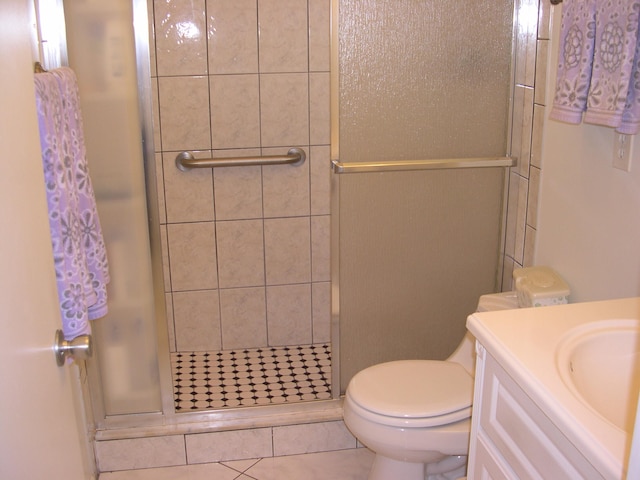 bathroom featuring tile patterned flooring, toilet, a shower with door, and vanity