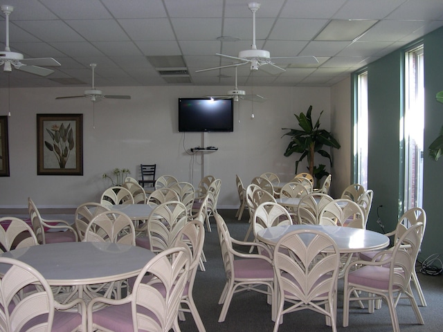 carpeted dining area with a paneled ceiling and ceiling fan