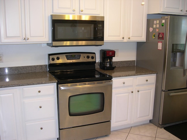 kitchen featuring dark stone countertops, light tile patterned floors, stainless steel appliances, and white cabinets