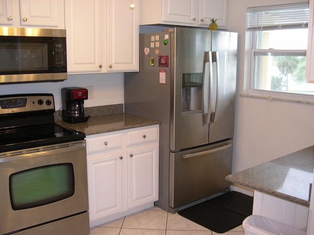 kitchen featuring white cabinets, appliances with stainless steel finishes, dark stone counters, and light tile patterned flooring