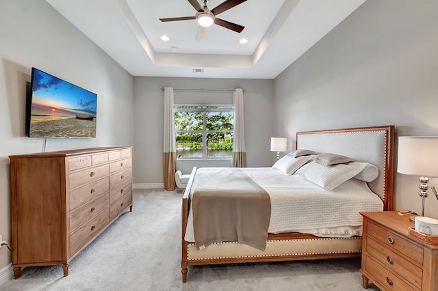 bedroom featuring light colored carpet, a raised ceiling, and ceiling fan