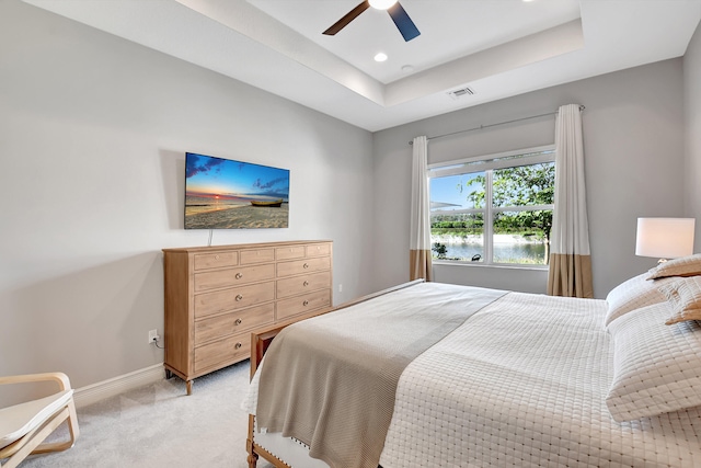 bedroom featuring light colored carpet, a raised ceiling, and ceiling fan