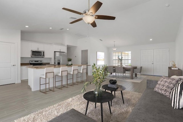 living room featuring ceiling fan, light hardwood / wood-style floors, sink, and vaulted ceiling