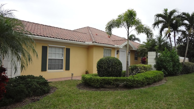 view of side of home featuring a yard, a tiled roof, and stucco siding