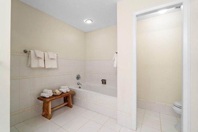 bathroom featuring toilet, a relaxing tiled tub, and tile patterned floors