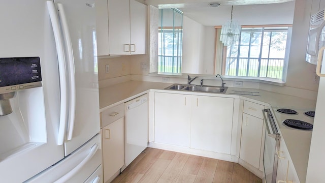 kitchen with white appliances, an inviting chandelier, sink, light hardwood / wood-style floors, and white cabinetry