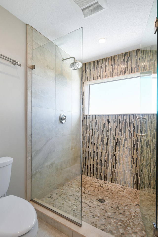 bathroom featuring walk in shower, tile patterned flooring, toilet, and a textured ceiling