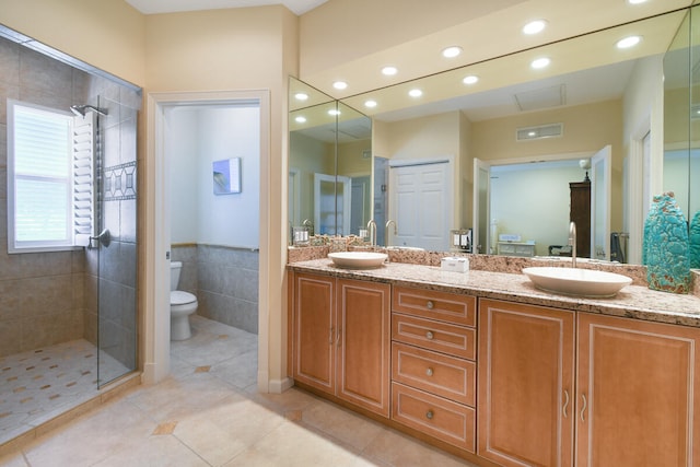 bathroom featuring double vanity, tile patterned flooring, toilet, and a tile shower